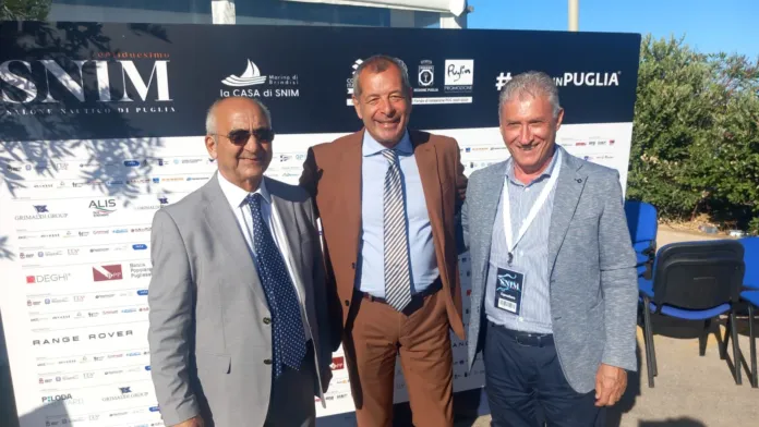 Tre persone in posa davanti a un pannello con la scritta SNIM e i loghi degli sponsor.