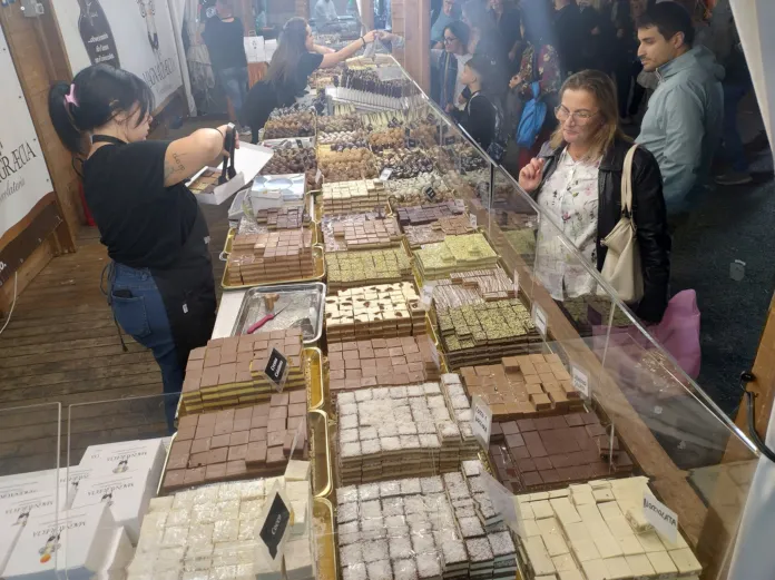 Banco con tavolette di cioccolato di diversi colori e persone davanti all’esposizione.