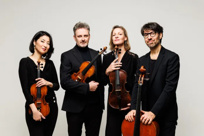 Immagine di archivio del Quartetto Prometeo con i quattro componenti in piedi e seduti con i loro strumenti, in un ambiente neutro.
