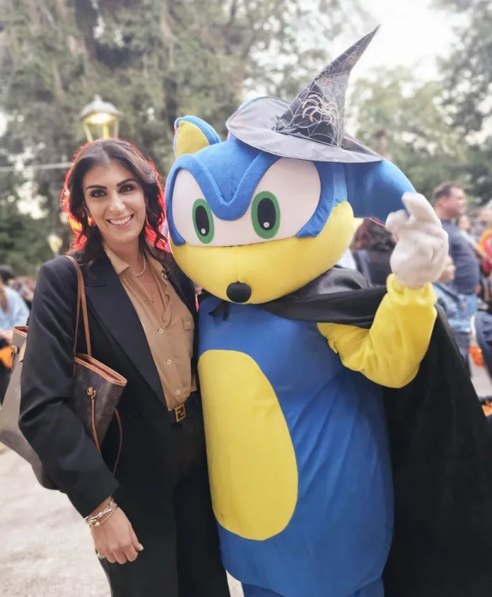 Una donna è accanto a una mascotte blu e gialla con cappello a punta e mantello scuro.