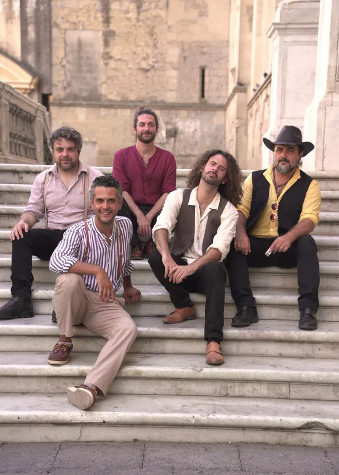 Foto della band La Terza Classe con strumenti musicali durante una posa in esterni su una scalinata in un contesto architettonico storico, immagine di archivio o illustrativa.