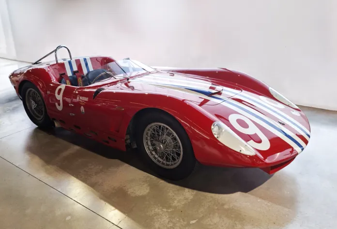 Vettura da corsa rossa con strisce bianche e blu e il numero 9, fotografata in un ambiente espositivo.