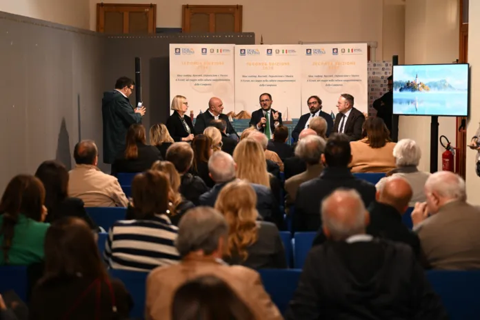 Persone sedute in sala ascoltano un gruppo di relatori durante un incontro; sullo sfondo sono visibili pannelli con il nome Praesentia.