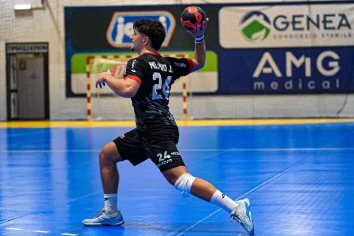 Un giocatore con maglia nera tiene una palla da pallamano mentre si prepara al tiro su un campo indoor.