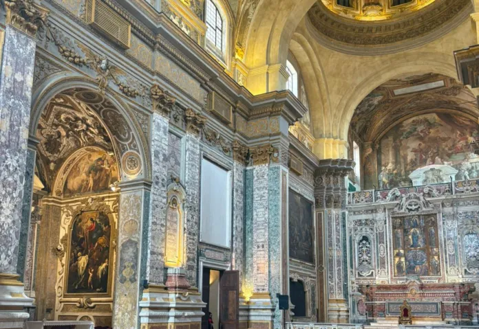 Veduta dell’interno di una chiesa con colonne, decorazioni e altare.