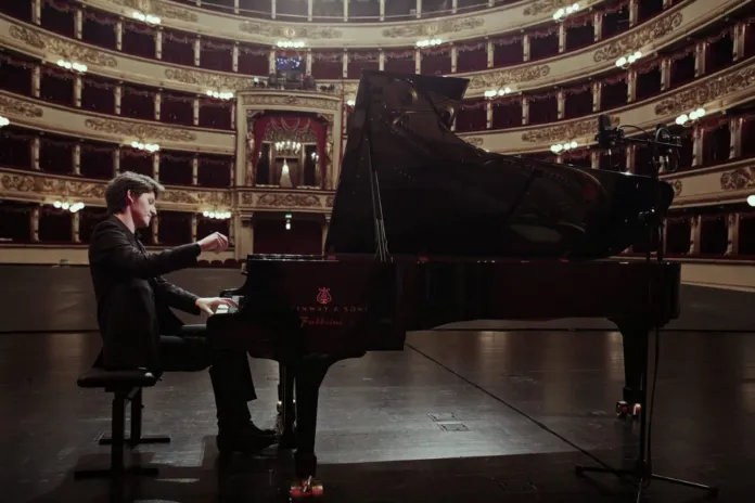 Foto di archivio di un pianista durante un concerto, con un grande teatro alle spalle.