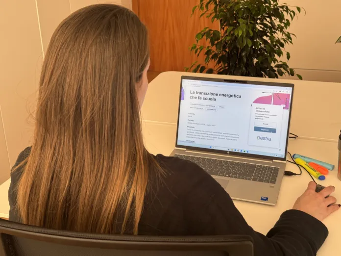 Una persona seduta davanti a un computer portatile, sul cui schermo è visibile una pagina intitolata «La transizione energetica che fa scuola».