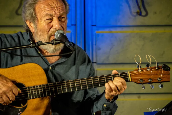 Foto di archivio di Edoardo De Angelis mentre si esibisce con chitarra e microfono in un locale, in un ambiente intimo e musicale.