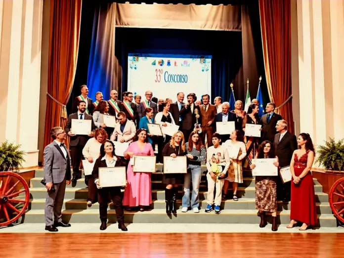 Persone con attestati posano sul palco, davanti a uno schermo e a diverse bandiere.