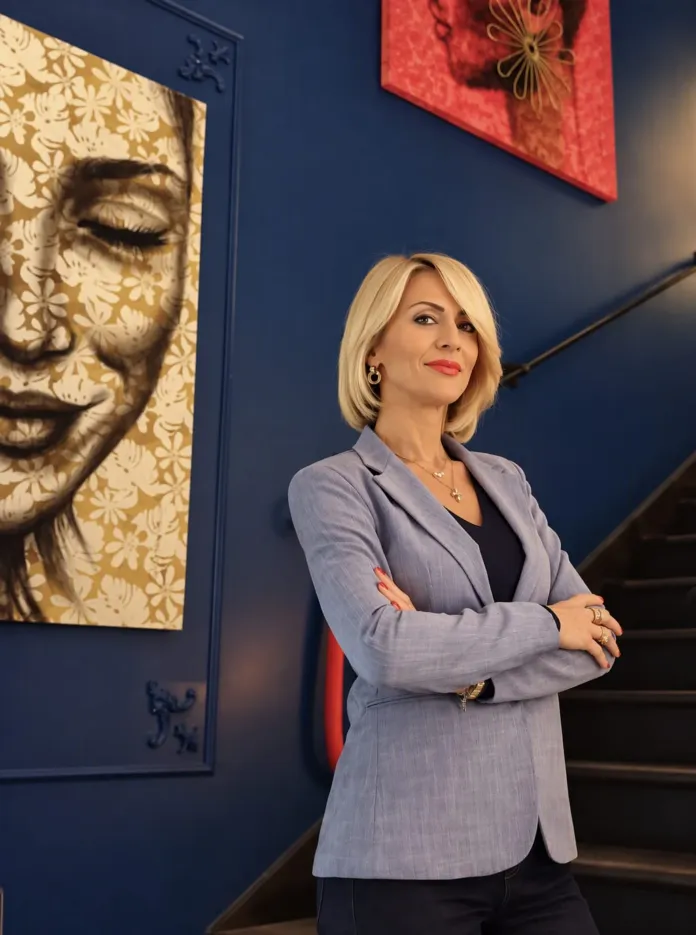 Una donna con giacca chiara è in piedi in una sala con opere d’arte alle pareti.