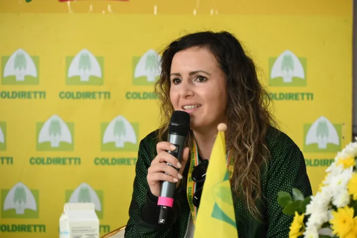 Foto di archivio di Veronica Barbati mentre parla al microfono durante un evento, con uno sfondo con il logo di Coldiretti.