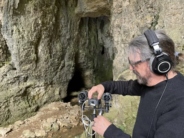 Una persona con cuffie regola un apparecchio di registrazione davanti a una cavità nella roccia.