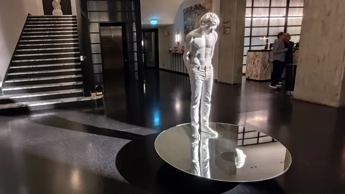 Scultura bianca moderna di un giovane uomo su una superficie specchiante nell'atrio di un edificio.