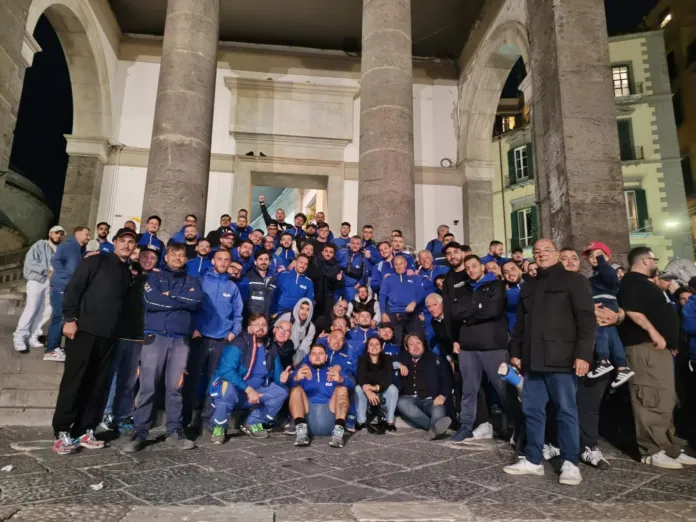 Un gruppo numeroso posa davanti a un edificio con colonne; molte persone indossano giacche blu.