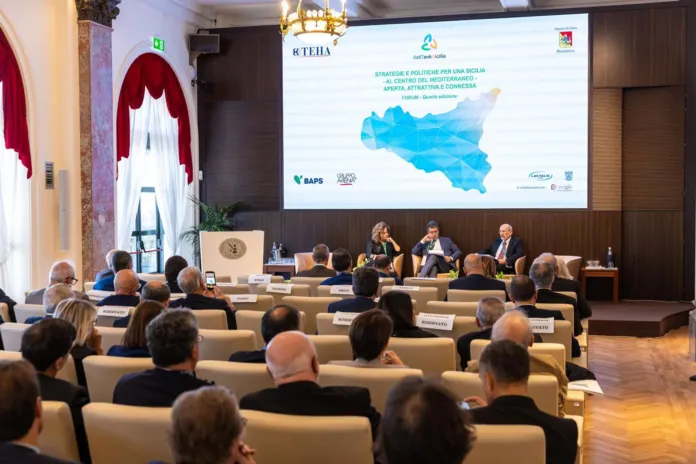 Sala con pubblico e relatori seduti a un tavolo; sullo schermo è proiettata una presentazione sulla Sicilia.