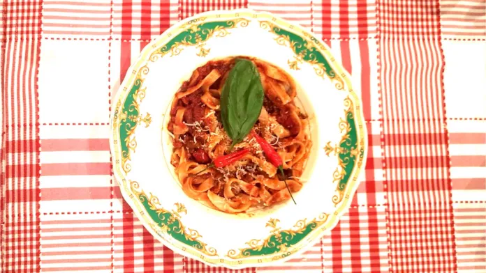 Piatto di pasta con sugo e una foglia di basilico, su una tovaglia a quadri rossi e bianchi.