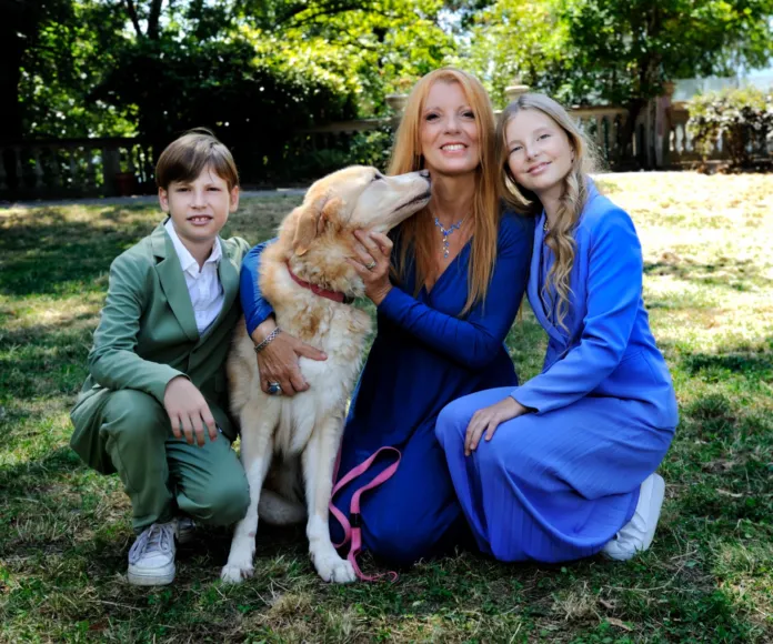 Immagine di archivio di una donna con un cane e due bambini, tutti sorridenti e in un giardino