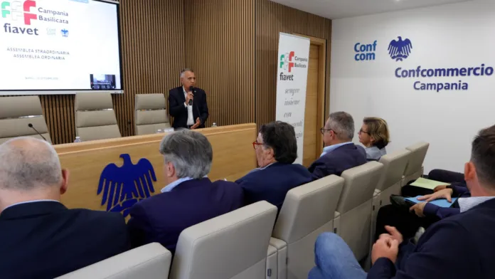 Una persona parla al microfono davanti a una platea seduta in una sala; alle pareti sono visibili i marchi FIAVET e Confcommercio Campania.