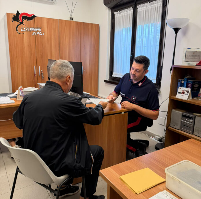 Ufficio dei Carabinieri con uomo che consegna documenti a un carabiniere seduto dietro una scrivania.