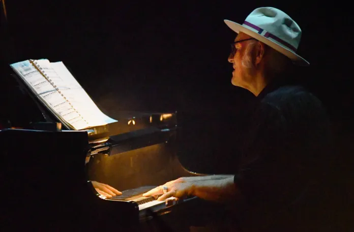 Immagine di un concerto di Ludovico Einaudi, pianista e compositore che suona al piano in scena, con un'illuminazione soffusa.