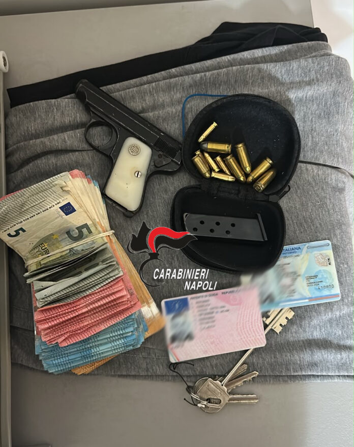 Pistola, munizioni, banconote, documenti contraffatti e altri oggetti disposti su una superficie grigia con il logo dei Carabinieri di Napoli.