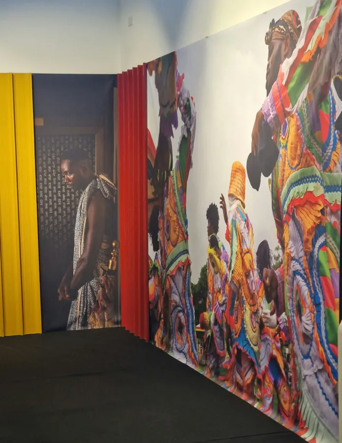 Allestimento della mostra con fotografie di persone e scene in abiti colorati esposte su pareti e pannelli.