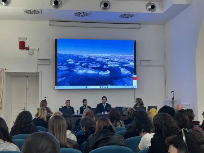 Una sala con il pubblico rivolto verso un tavolo di relatrici e relatori; sullo schermo è proiettata una veduta del mare.