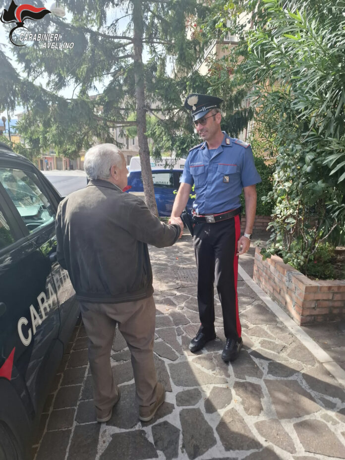 Carabiniere e anziano si stringono la mano vicino a un'auto dei Carabinieri in un ambiente urbano.