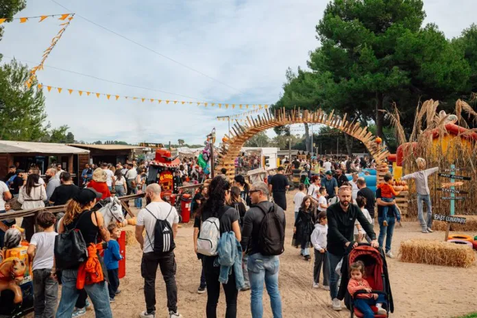 Folla di persone in un parco decorato per una festa autunnale con zucche e decorazioni tipiche.