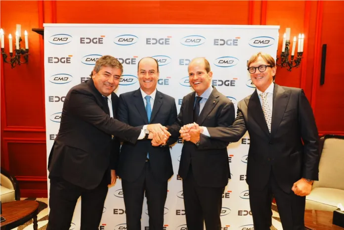 Quattro uomini in abito formale posano stringendosi la mano davanti a un fondale con i loghi CMD ed EDGE.