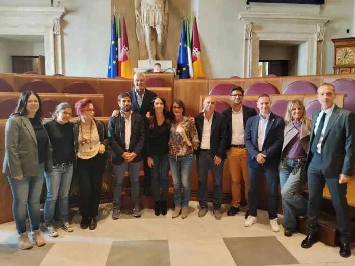 Immagine di archivio che mostra un gruppo di persone all'interno di un'aula parlamentare, sedute e in piedi, con bandiere in backgrounds.