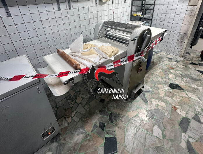 Laboratorio di pasticceria con attrezzature sequestrate e nastro dei Carabinieri a Napoli.