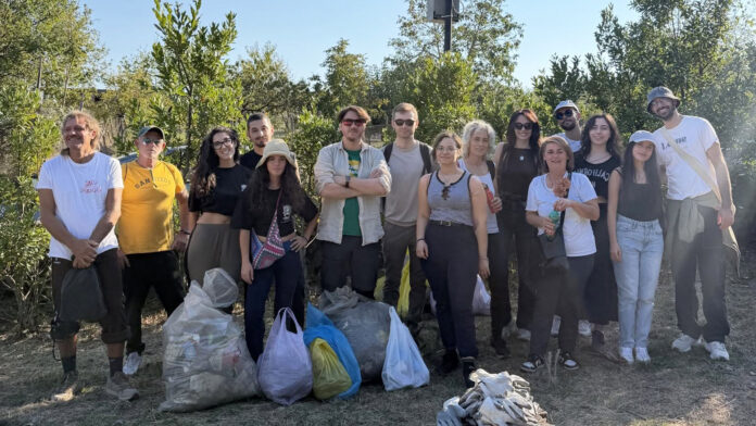 Foto di un gruppo di volontari in piedi all'aperto accanto a sacchi contenenti rifiuti raccolti durante l'attività di pulizia della pineta a Terzigno.