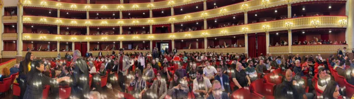 Pubblico seduto in platea in un teatro con palchi.