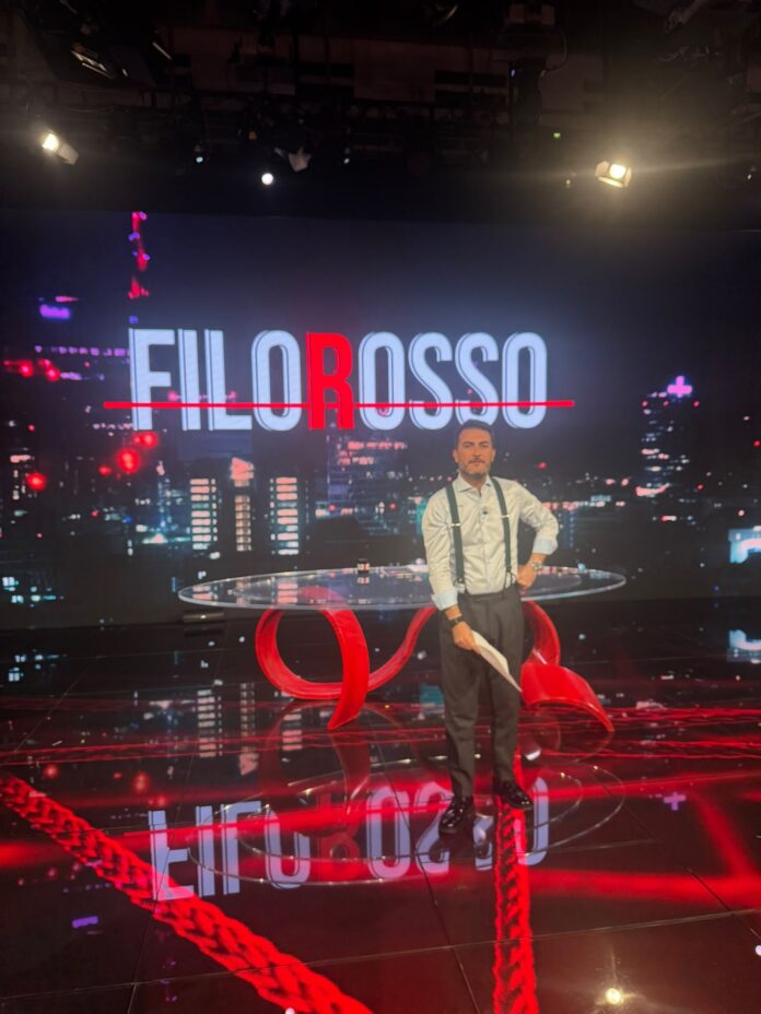 Antonino Monteleone nello studio di registrazione di Filorosso, Rai 3, in piedi davanti al logo della trasmissione.