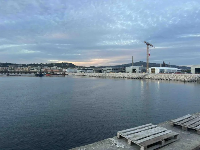 Specchio d’acqua in primo piano; sulla riva si vedono edifici e una gru.