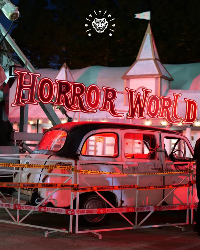 Scenografia notturna con insegna “Horror World”, un’automobile e transenne.