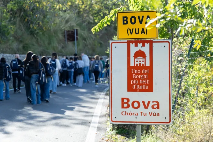 Un gruppo di persone con zaini cammina lungo una strada. In primo piano si vede un cartello con la scritta «Bova».
