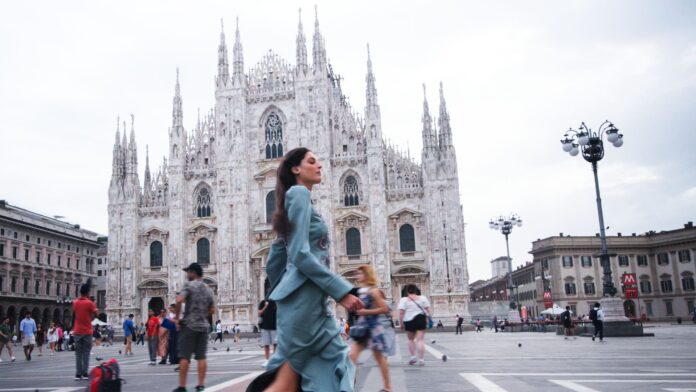 Donna elegante cammina con il Duomo di Milano sullo sfondo in una giornata affollata.