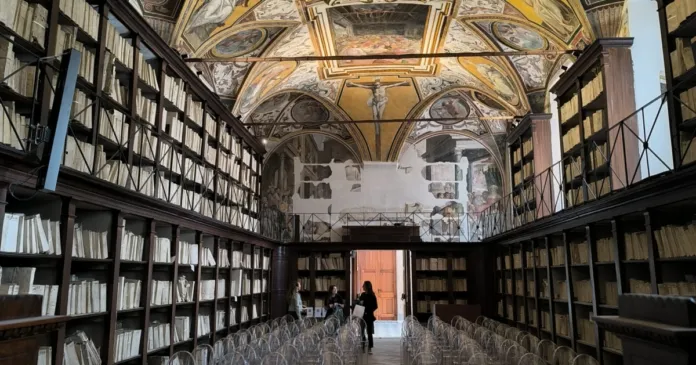 Sala interna dell'Archivio di Stato di Napoli con scaffali pieni di documenti e un soffitto affrescato.