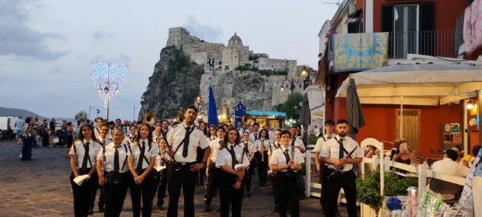 Banda musicale in marcia a Ischia con il castello aragonese sullo sfondo, immagine di archivio del festival musicale.