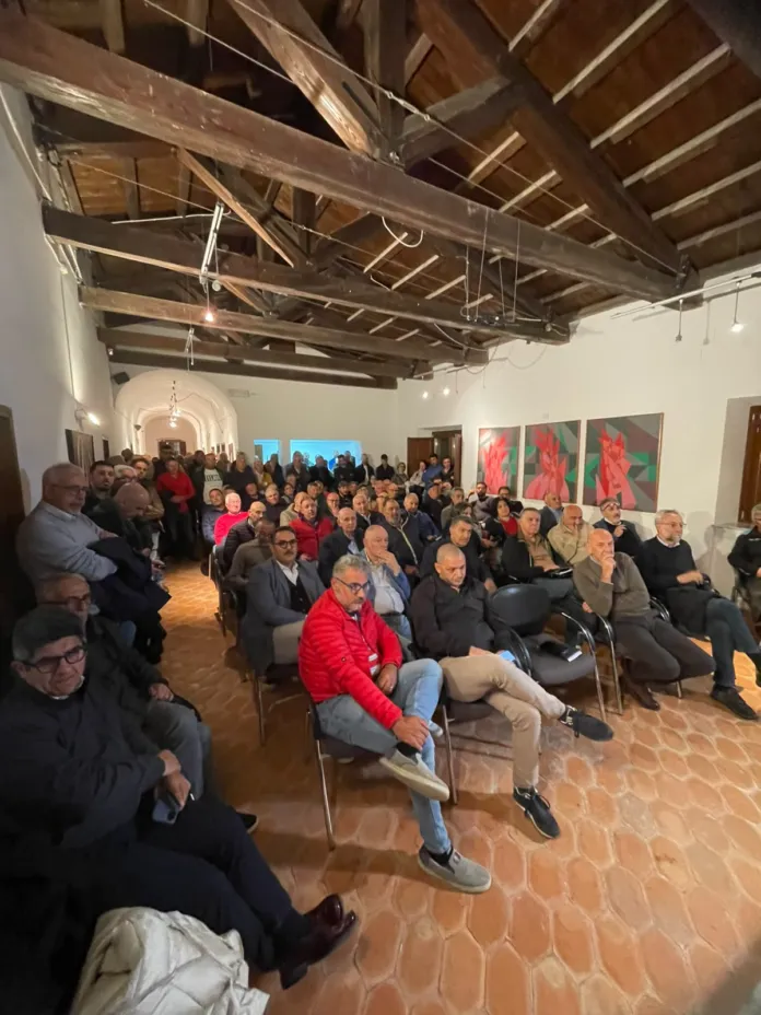 Persone sedute in una sala, rivolte verso chi parla fuori campo.