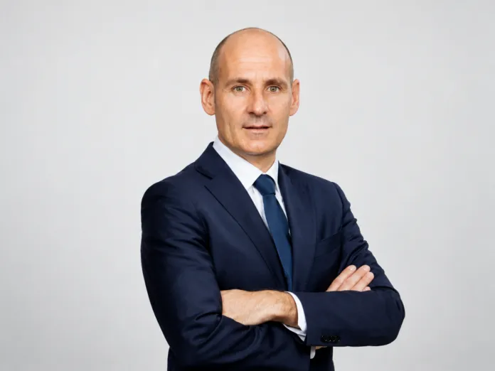 Immagine di Hernan Bassi in abito formale, con le braccia incrociate, sfondo bianco.