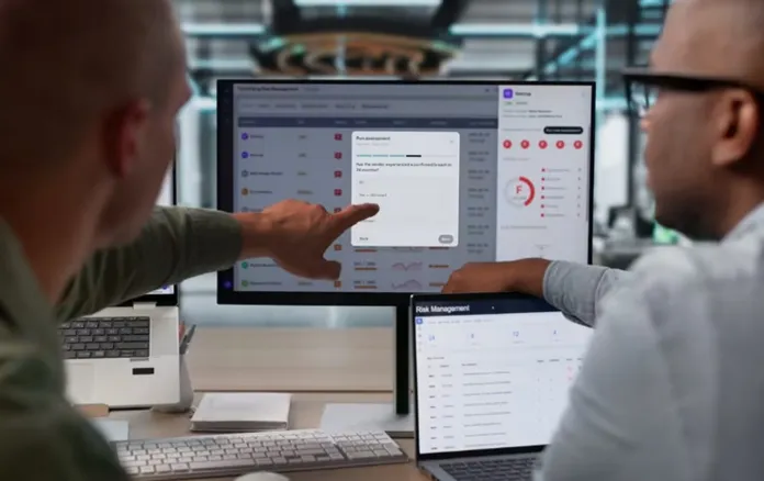 Fotografia di archivio di due professionisti che discutono di sicurezza informatica davanti a monitor con dati e grafici.