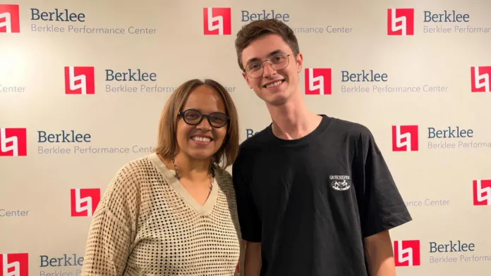 Un uomo con occhiali e una donna sorridono in posa davanti a uno sfondo con loghi e scritte Berklee.