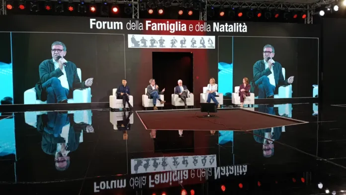 Palco con diverse persone sedute e la scritta «Forum della Famiglia e della Natalità» sullo schermo.