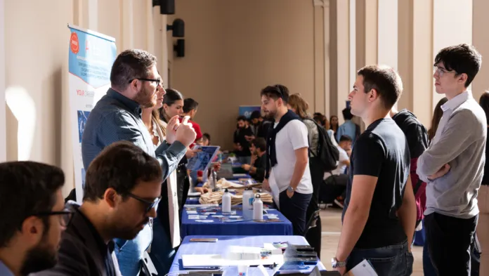 Persone in conversazione davanti a banchi informativi durante un career day.