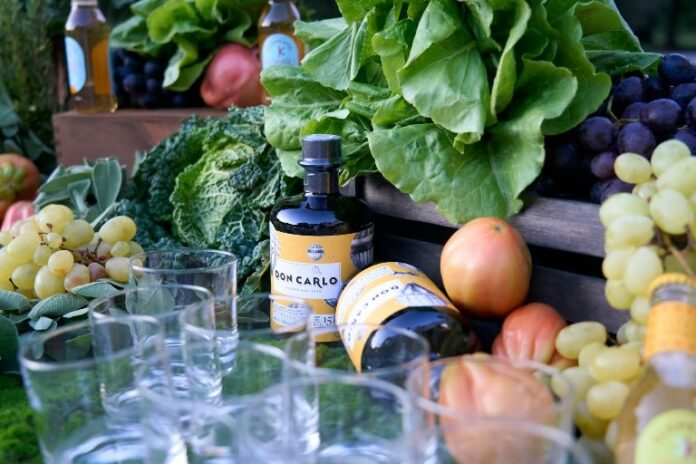 Bottiglie di Amaro Don Carlo con bicchieri e verdure in esterno.