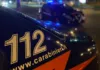 Carabinieri denunciano un 21enne per danneggiamento a Frattamaggiore Dettaglio della fiancata di un’auto dei Carabinieri con la scritta 112; sullo sfondo si vede un altro veicolo con luci blu.