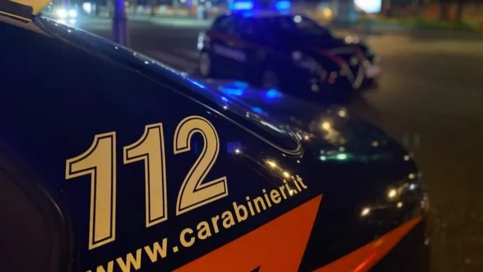 Dettaglio della fiancata di un’auto dei Carabinieri con la scritta 112; sullo sfondo si vede un altro veicolo con luci blu.